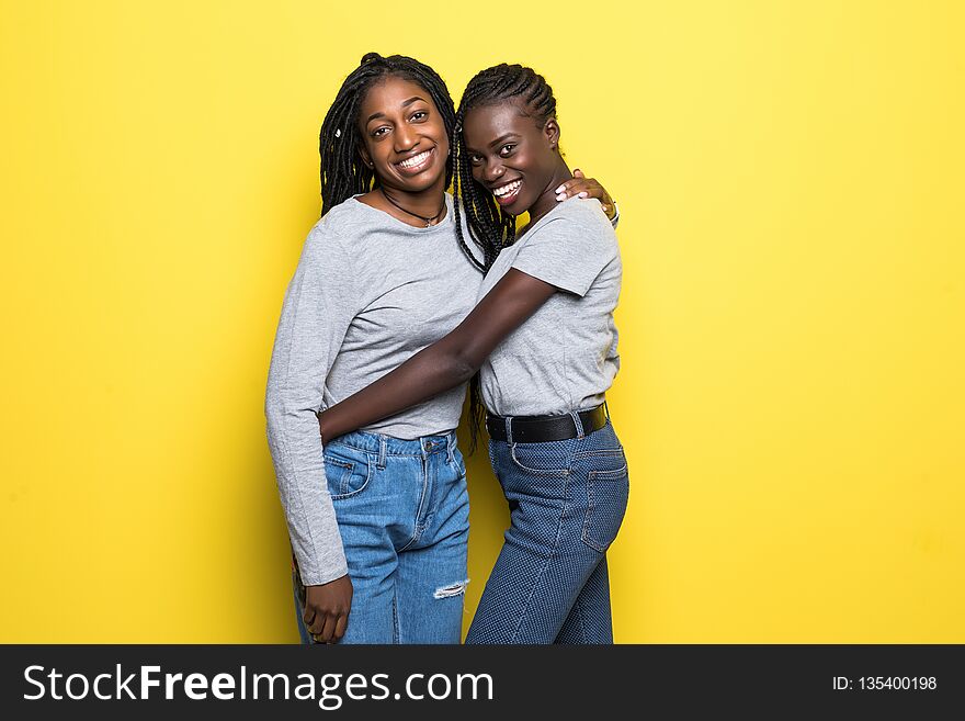 Photo of lovely african womens stand closely hug each other embrace isolated over yellow background. People and diversity concept. Photo of lovely african womens stand closely hug each other embrace isolated over yellow background. People and diversity concept