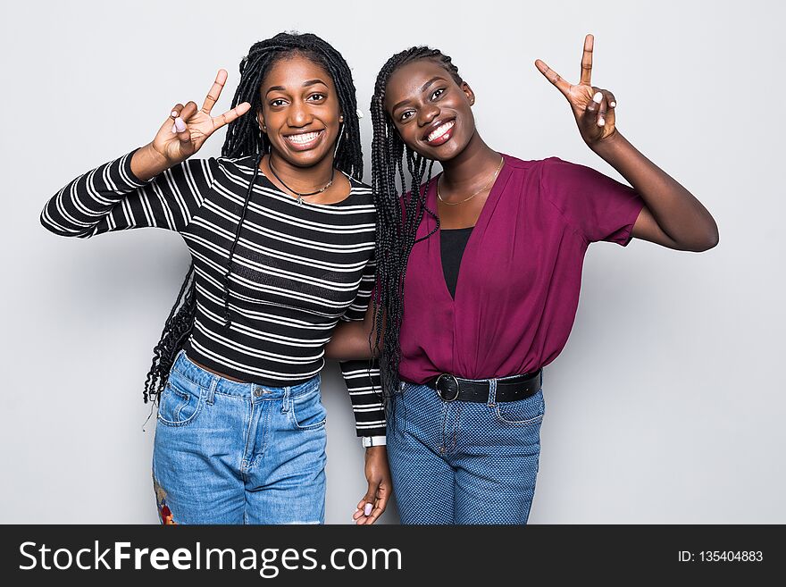 Portrait of a two african girlfriends showing two fingers sign on gray background