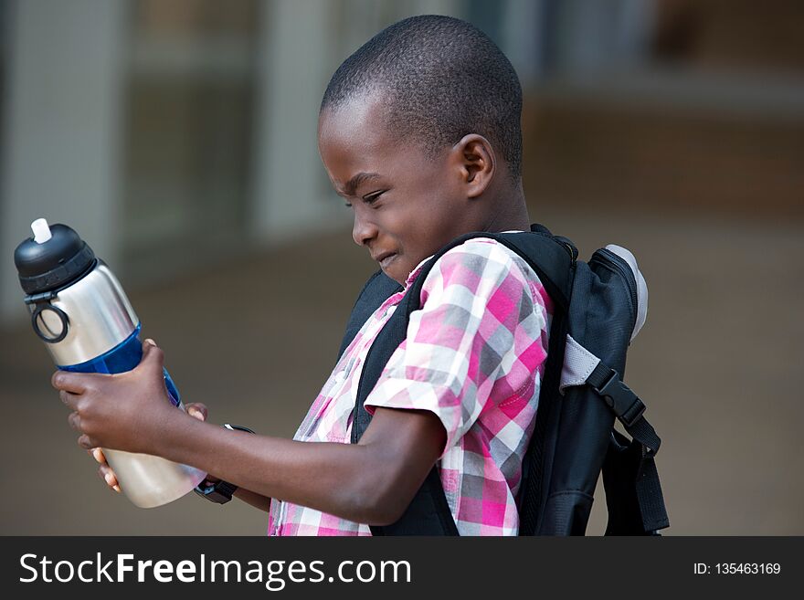 Schoolboy looking and trying to open his bottle of water that he holds in his hands. Schoolboy looking and trying to open his bottle of water that he holds in his hands