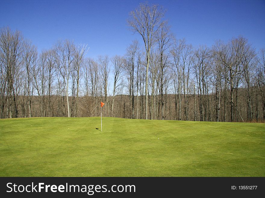 A golf green with a red flag, golf ball and blue sky background. Taken at Pinecroft Golf Course, Beulah, Michigan. A golf green with a red flag, golf ball and blue sky background. Taken at Pinecroft Golf Course, Beulah, Michigan.