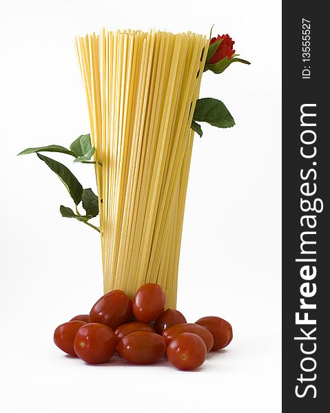 Raw spaghetti standing with tomatoes on the base and a flowered red rose up. Raw spaghetti standing with tomatoes on the base and a flowered red rose up