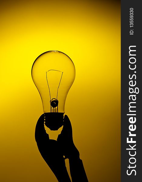 A silhouette of a clear light bulb held in a grip on a yellow glow background. A silhouette of a clear light bulb held in a grip on a yellow glow background