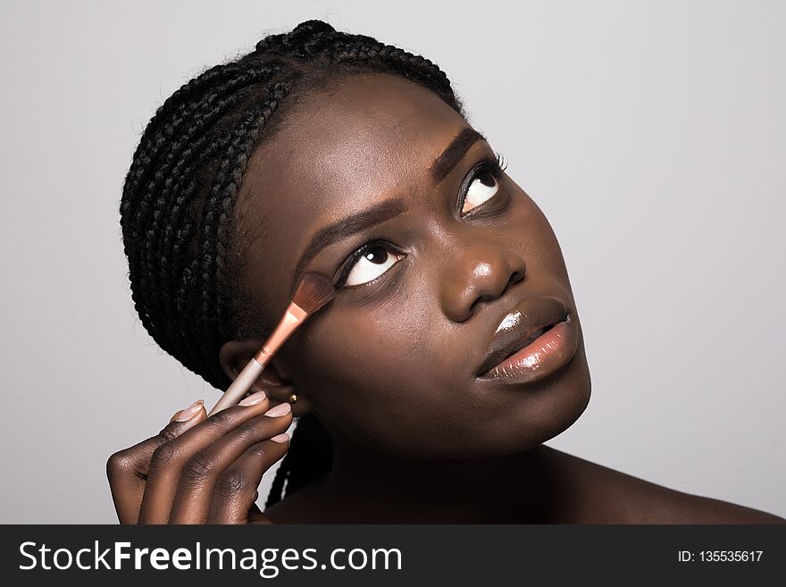 Portrait of beautiful afro american woman applying cosmetic isolated on beige isolated on white