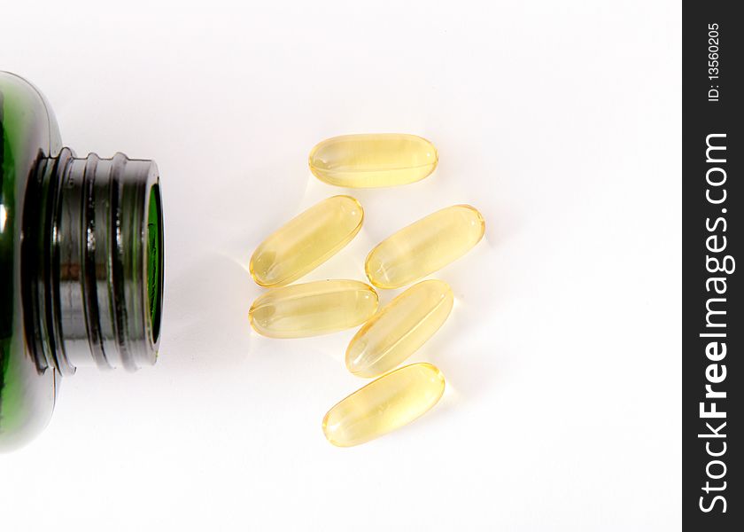 Yellow pills and green bottle on light background