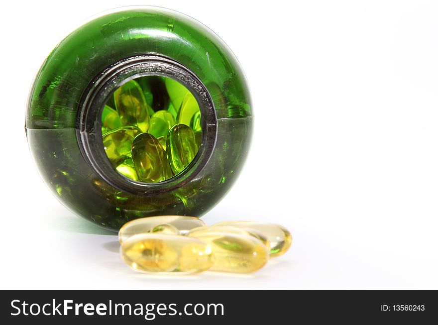 Yellow pills and green bottle on light background