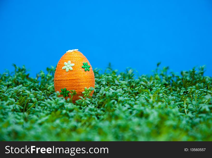 Handmade easter egg dropped on cress. Small eggs are covered by cotton string in different colours. Additional decorative elements are glued to egg. Blue background. Handmade easter egg dropped on cress. Small eggs are covered by cotton string in different colours. Additional decorative elements are glued to egg. Blue background.