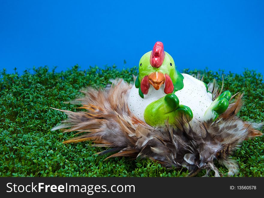 Big ceramic hen in feather nest, lying on cress. Ceramic hen is used as Easter decoration. Big ceramic hen in feather nest, lying on cress. Ceramic hen is used as Easter decoration