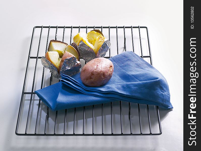 One whole and two jacket potatoes with blue serviette ,all on stainless steel grille.