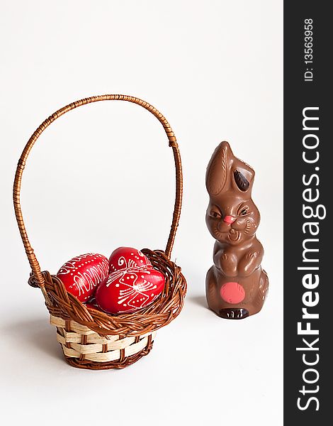 Milk chocolate bunny and red Easter eggs in a basket on white background. Milk chocolate bunny and red Easter eggs in a basket on white background