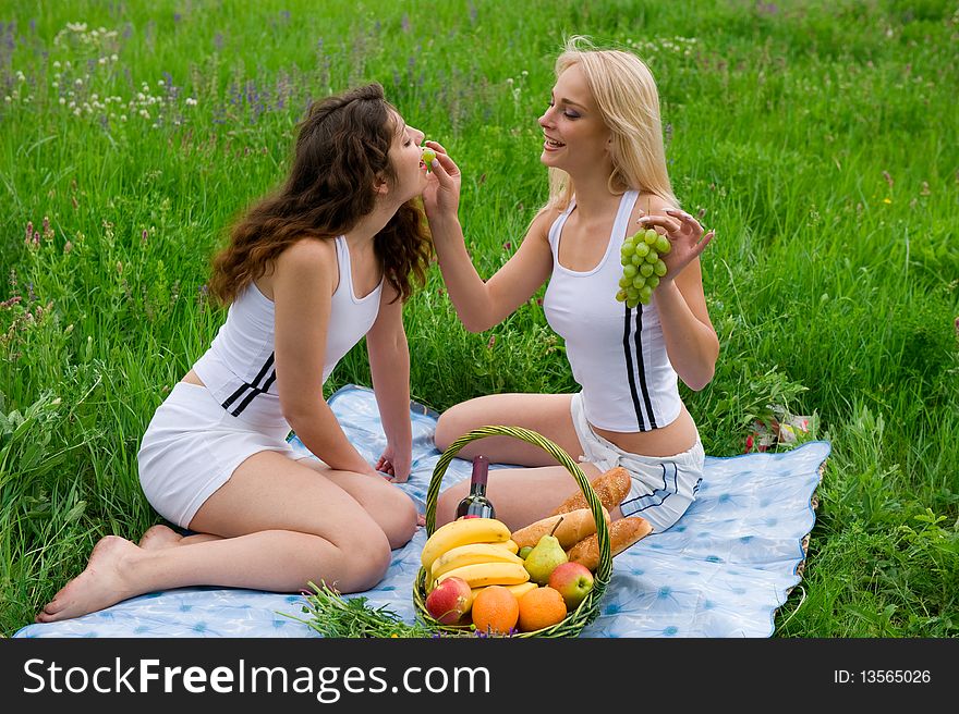 Two beautiful girls blonde and brunette in white suits, feed each other grapes. Two beautiful girls blonde and brunette in white suits, feed each other grapes