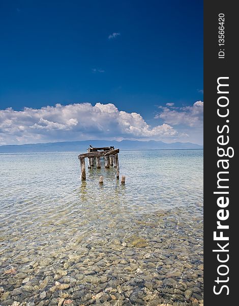 Decayed jetty in a lake blue skies clear water with pebbles