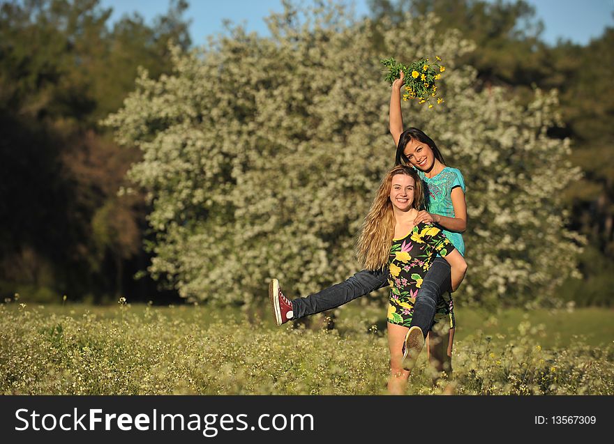 Two Beautiful Young Women Piggy-backing In Meadow