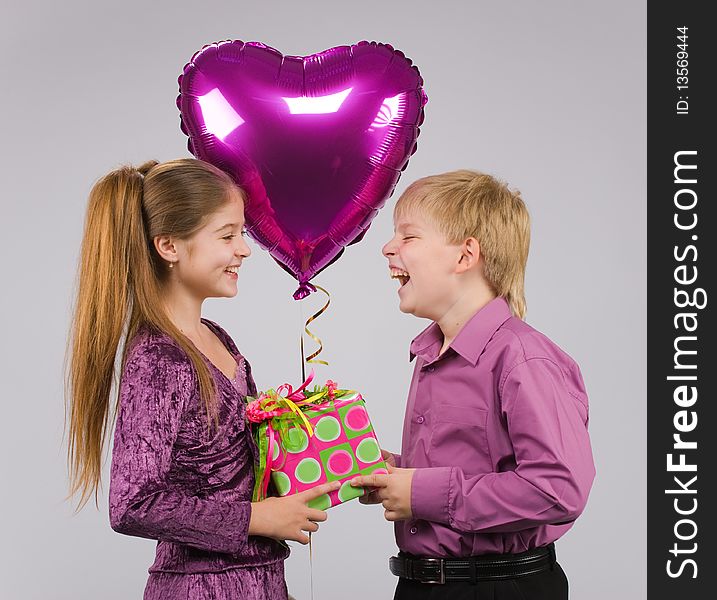 Boy and girl stand facing each other with a gift and a balloon in hand. Boy and girl stand facing each other with a gift and a balloon in hand