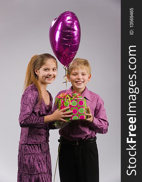 Boy and girl stand facing each other with a gift and a balloon in hand. Boy and girl stand facing each other with a gift and a balloon in hand