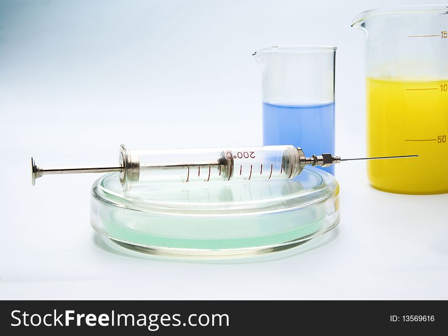 Transparent chemical glassware with green, yellow and blue solution with syringe. Transparent chemical glassware with green, yellow and blue solution with syringe