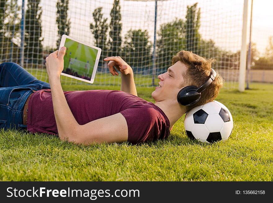 Teenager laying on grass with soccer ball behind his neck