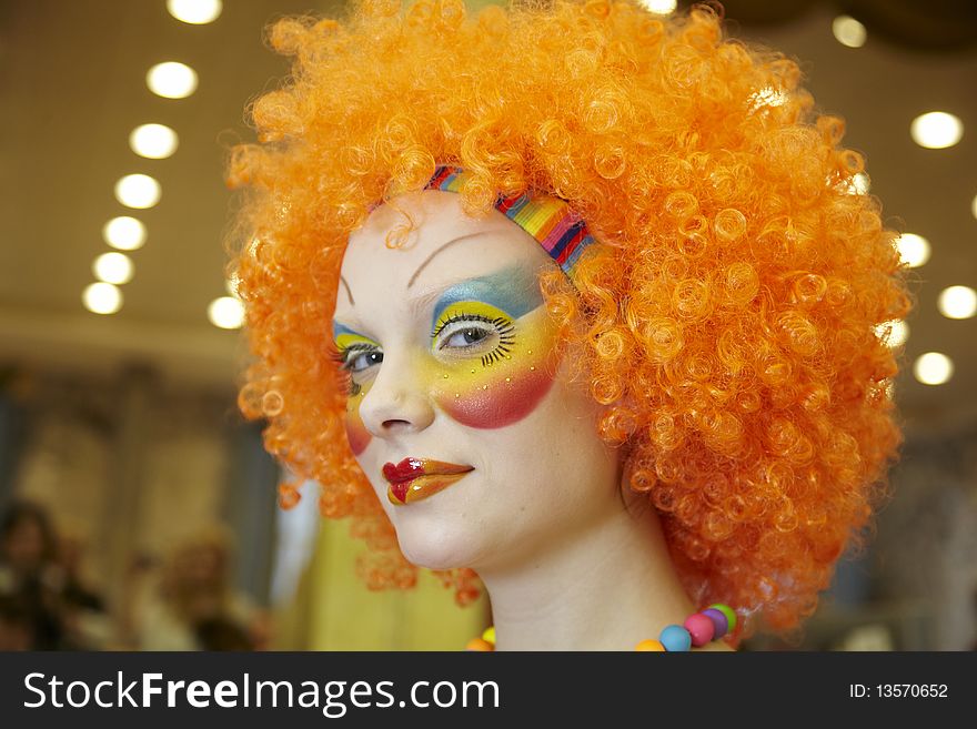 The young, beautiful girl in an image of the clown with an is bright-red wig and in a make-up. The young, beautiful girl in an image of the clown with an is bright-red wig and in a make-up