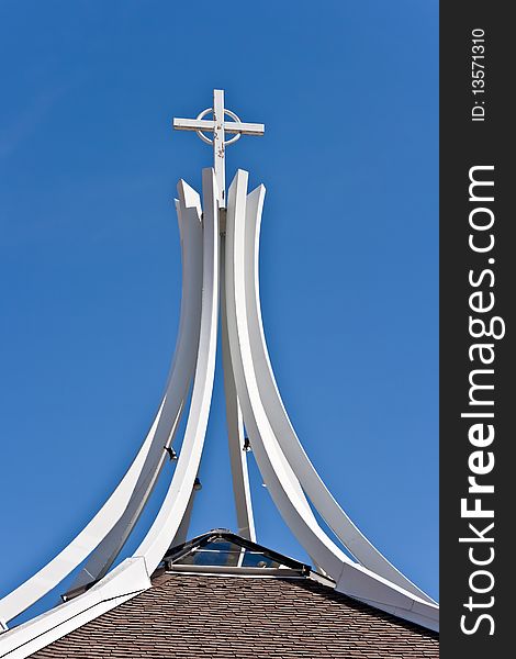 Under a clear blue sky, a cross is supported by curved beams on top of a church. Under a clear blue sky, a cross is supported by curved beams on top of a church.