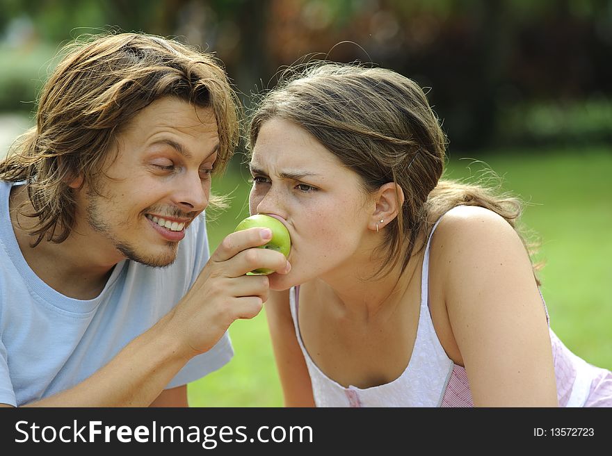 Happy healthy attractive couple with their apple in the park. Happy healthy attractive couple with their apple in the park