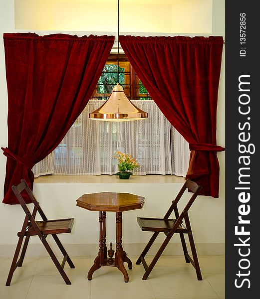 A beautifully lit window overlooking antique wooden chairs and table. An overhead reading lamp. A beautifully lit window overlooking antique wooden chairs and table. An overhead reading lamp.