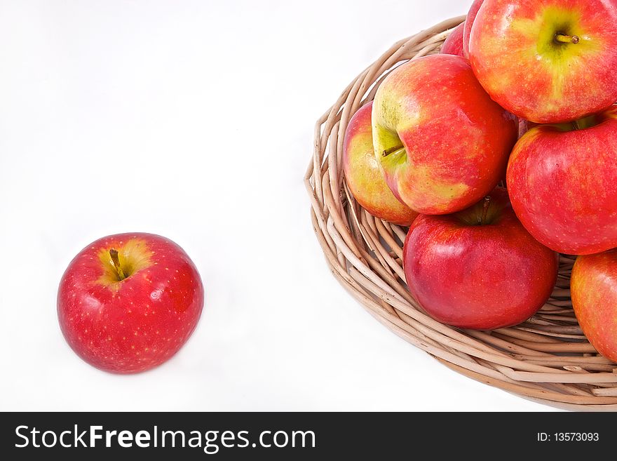 Red apples on a basket and one rolled away on white backround