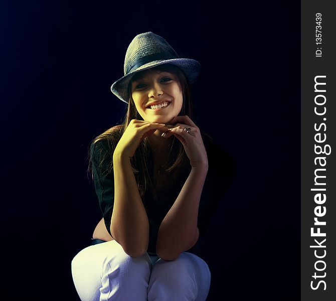 Young girl sitting with hat on head and hands with shape heart on dark backgrounds. Young girl sitting with hat on head and hands with shape heart on dark backgrounds