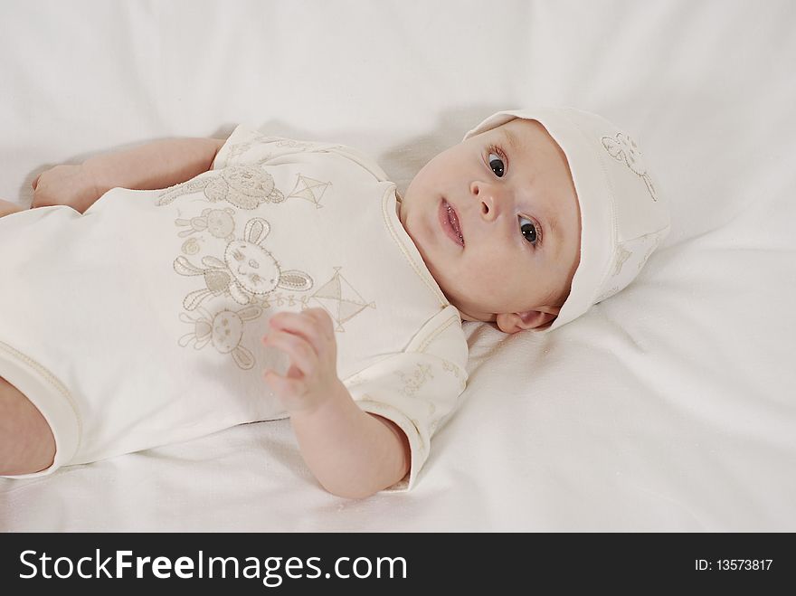 Satisfied baby lying on a bed in the white hat