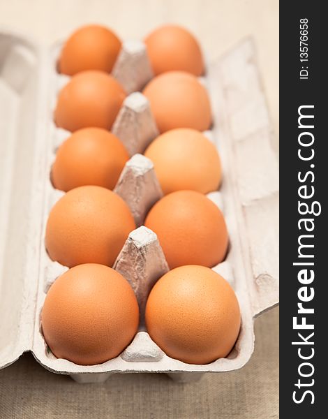 Open cardboard eggbox with ten brown eggs. Shallow dof, focus is on front eggs. Open cardboard eggbox with ten brown eggs. Shallow dof, focus is on front eggs.
