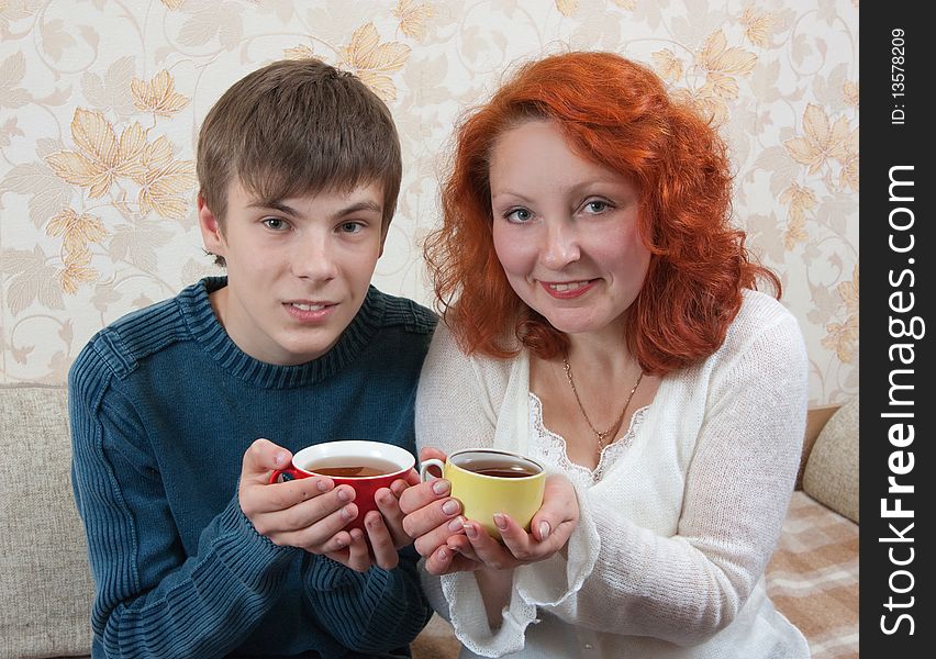 Smiling woman and teen boy have tea on sofa at home. Smiling woman and teen boy have tea on sofa at home