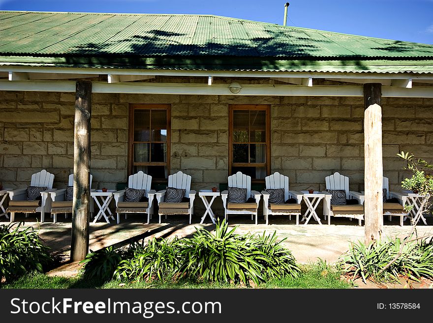 Perspective shot of many white wooden chairs on veranda of old stone building in shade to rest and relax. Perspective shot of many white wooden chairs on veranda of old stone building in shade to rest and relax