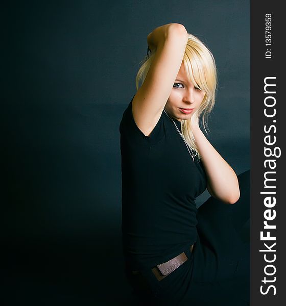 Portrait of a beautiful black dressed blonde, she is sitting in a studio with her arms touching her head. Portrait of a beautiful black dressed blonde, she is sitting in a studio with her arms touching her head