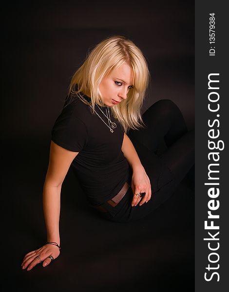 Portrait of a beautiful black dressed blonde, she is sitting in a studio with black background