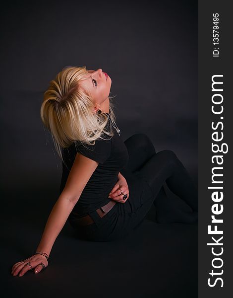 Portrait of a beautiful black dressed blonde in a studio, she is sitting and throwing back her head. Portrait of a beautiful black dressed blonde in a studio, she is sitting and throwing back her head