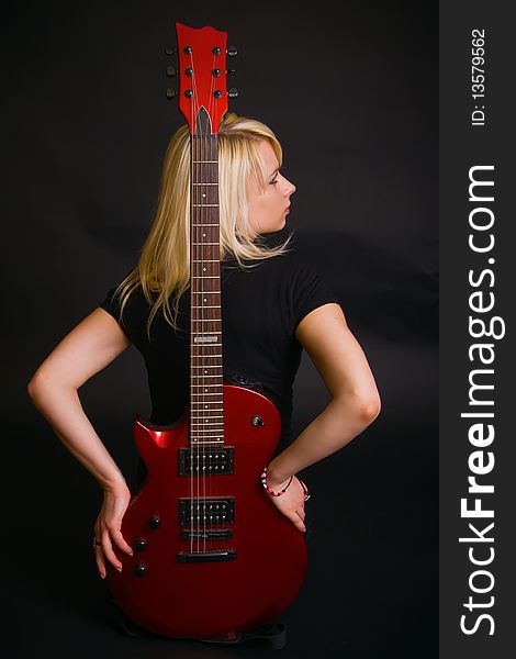 Beautiful slim blonde in black dress holding a red guitar. Beautiful slim blonde in black dress holding a red guitar