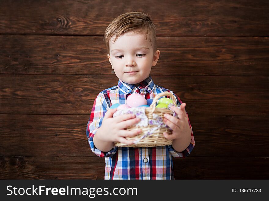 Happy baby boy with a basket of eggs on a wooden wall background