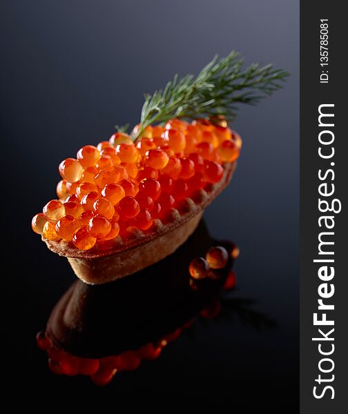 Canape with red caviar on a black reflective background