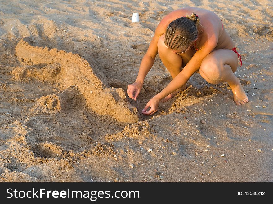 The girl on the beach makes the crocodile out of the sand. The girl on the beach makes the crocodile out of the sand