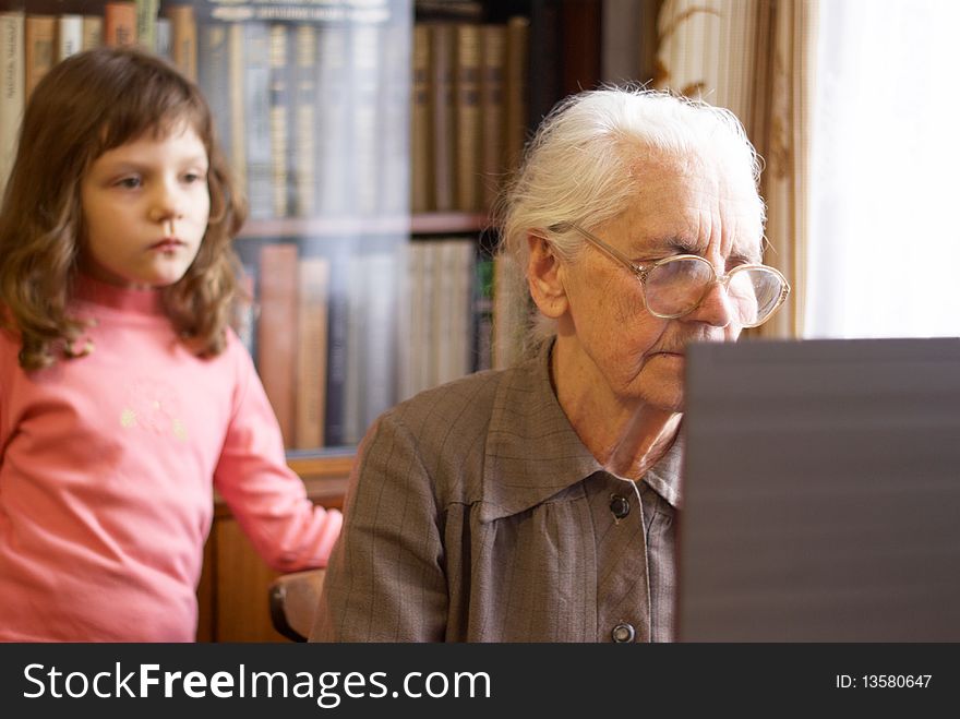 Great-grandmother working with laptop and granddoughter  standing behind. Great-grandmother working with laptop and granddoughter  standing behind