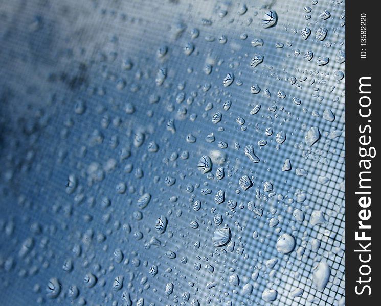 Close-up of rain drops on window with blue sky and screen bhind. Close-up of rain drops on window with blue sky and screen bhind