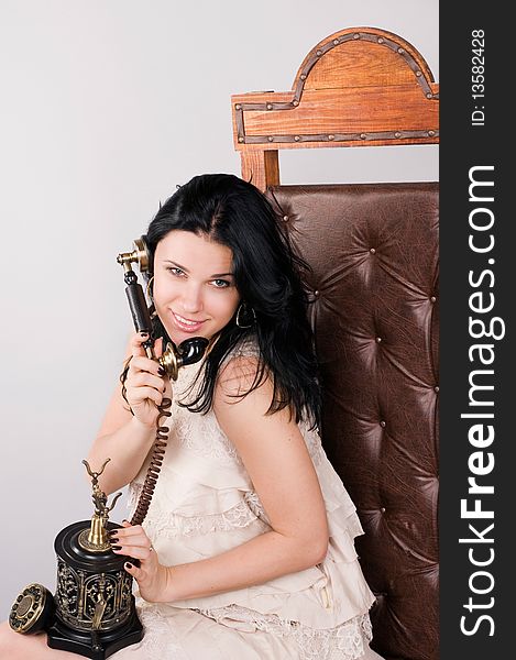 Beautiful woman sits on a chair and speaks by ancient phone. Beautiful woman sits on a chair and speaks by ancient phone.
