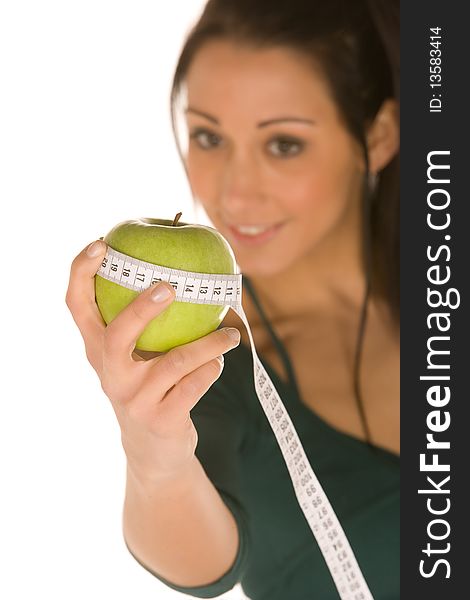 Young caucasian brunette blurred,holds a granny smith apple and a measuring tool in focus. Young caucasian brunette blurred,holds a granny smith apple and a measuring tool in focus