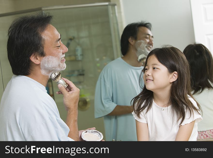 Daughter watching father apply shaving cream in bathroom. Daughter watching father apply shaving cream in bathroom