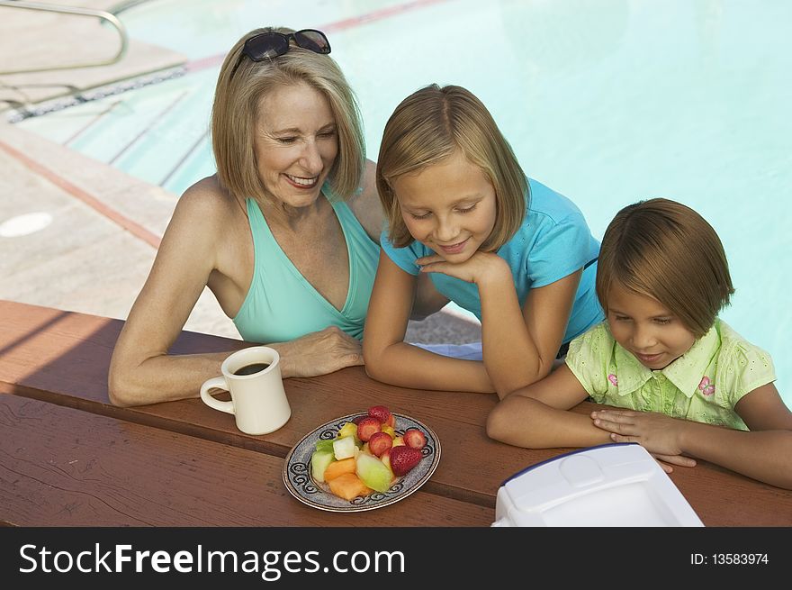 Two Girls (7-9) and Grandmother Watching portable television by swimming pool. Two Girls (7-9) and Grandmother Watching portable television by swimming pool.