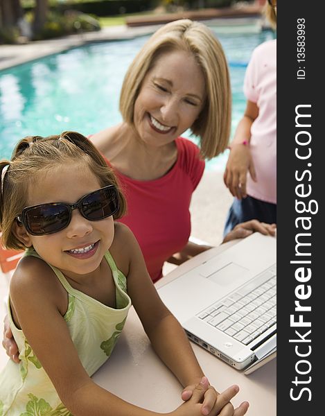 Two girls (7-9) using laptop with grandmother by swimming pool, portrait. Two girls (7-9) using laptop with grandmother by swimming pool, portrait.