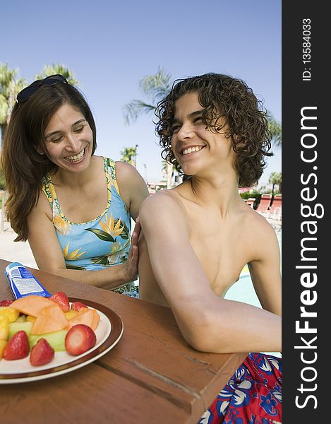 Woman applying sunscreen to son (13-15) at swimming pool.