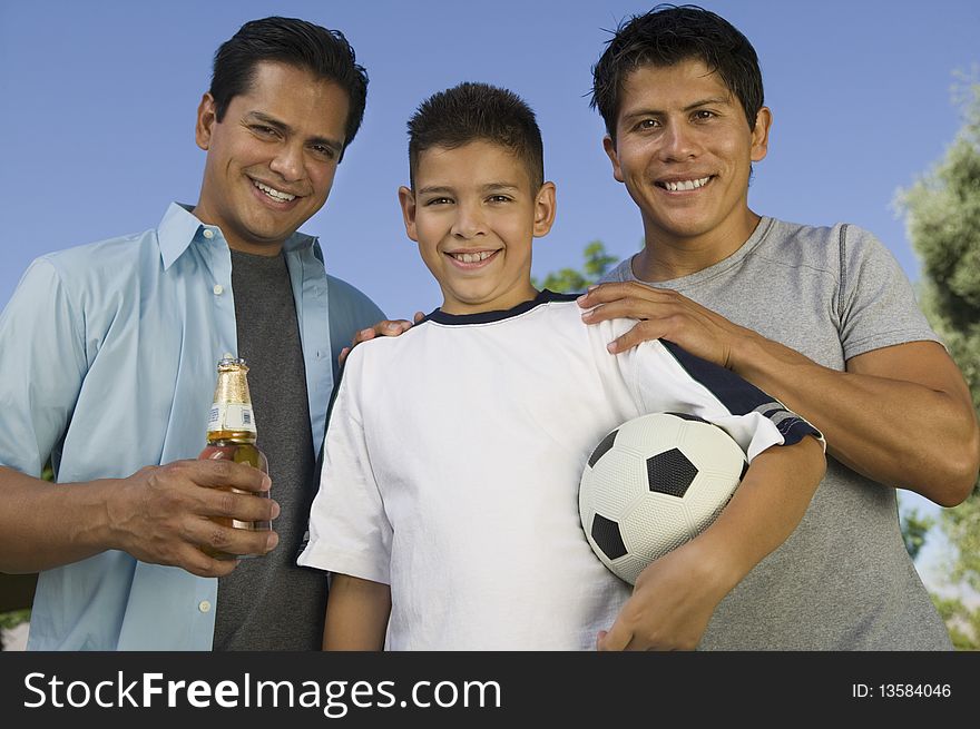 Boy (13-15) holding soccer ball, standing with two brothers, one brother holding beer bottle, front view. Boy (13-15) holding soccer ball, standing with two brothers, one brother holding beer bottle, front view.