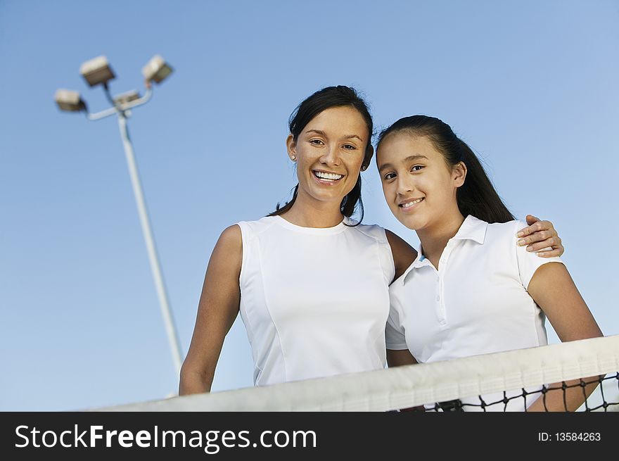 Mother and daughter standing at net on tennis court, portrait, low angle view. Mother and daughter standing at net on tennis court, portrait, low angle view