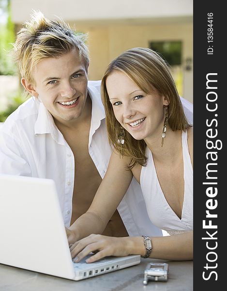 Couple Sitting At Backyard Table Using Laptop