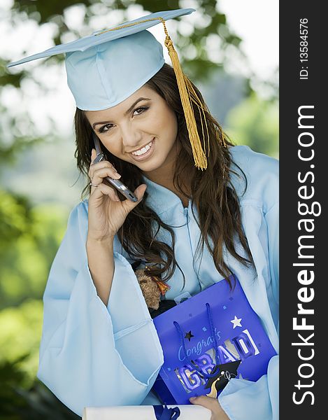 Graduate Using Cell Phone And Holding Gift Bag