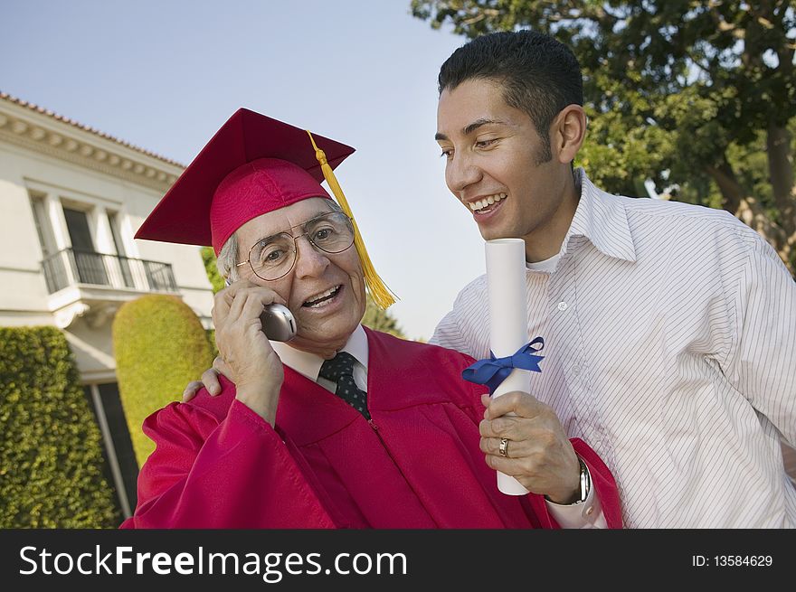 Senior Graduate using cell phone outside with son, low angle view